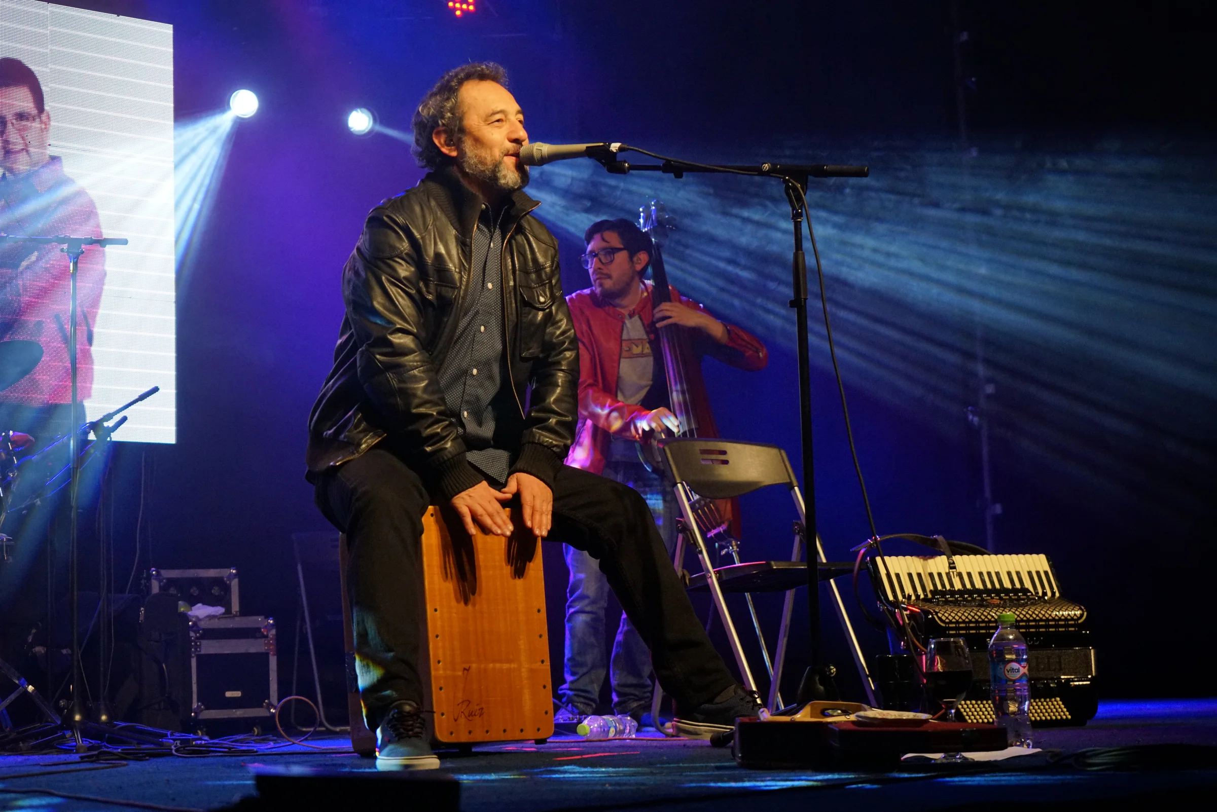 Músico cantando y tocando cajón en vivo con iluminación escénica