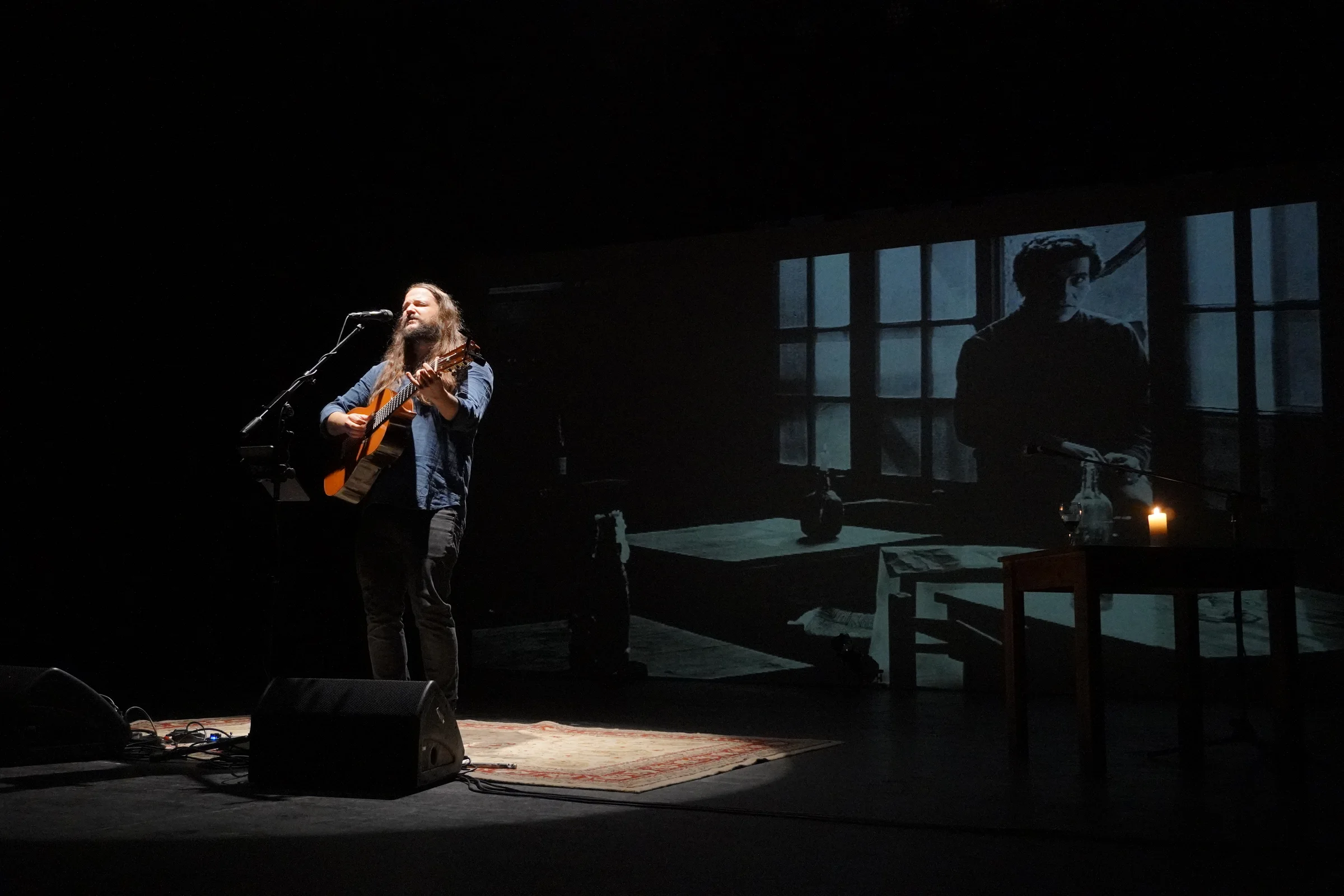 Cantautor con guitarra acústica en escenario teatral bajo foco cenital