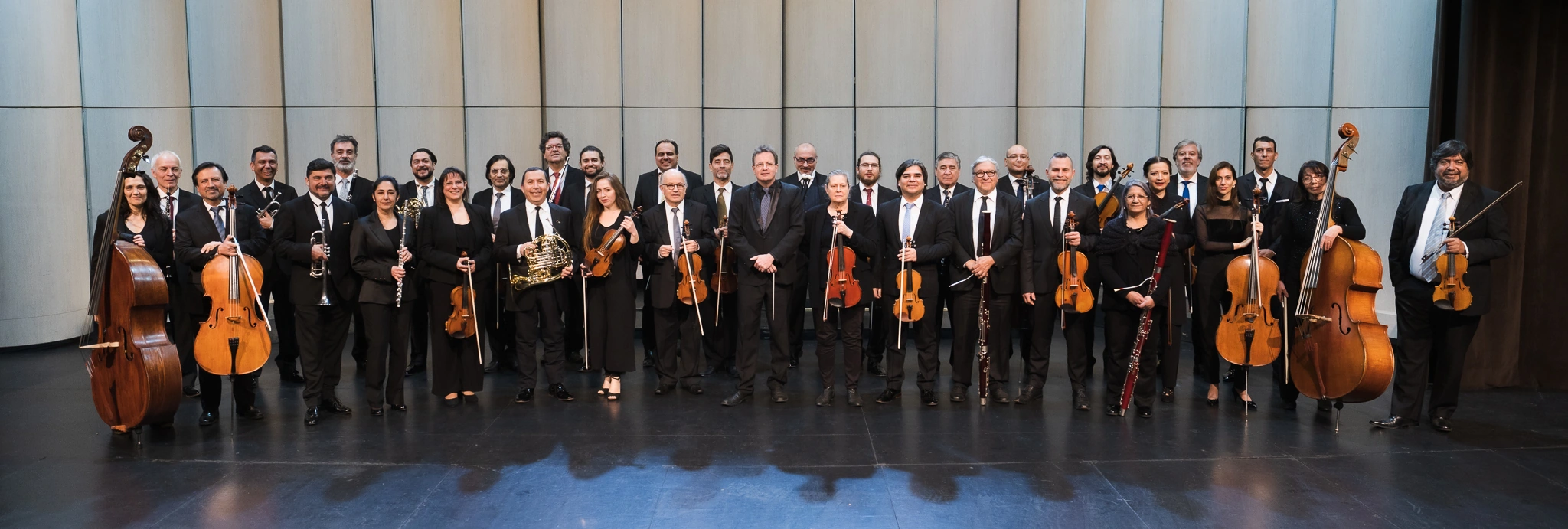 Orquesta de cámara posando en escenario con instrumentos musicales