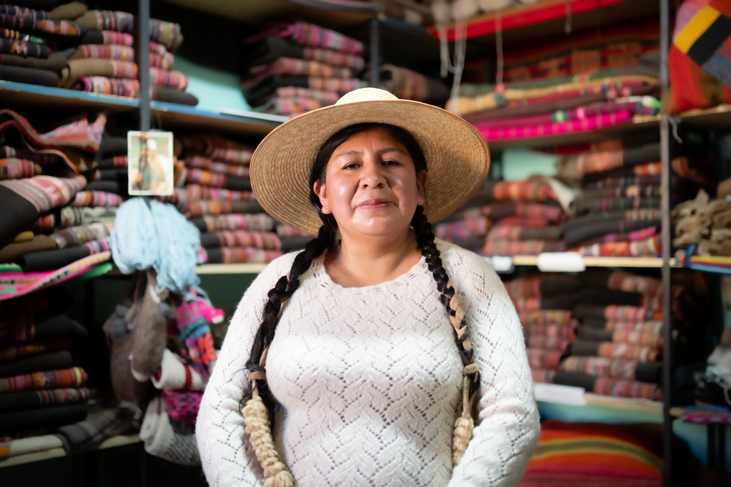 Artesana textil andina posando frente a estantes con tejidos tradicionales