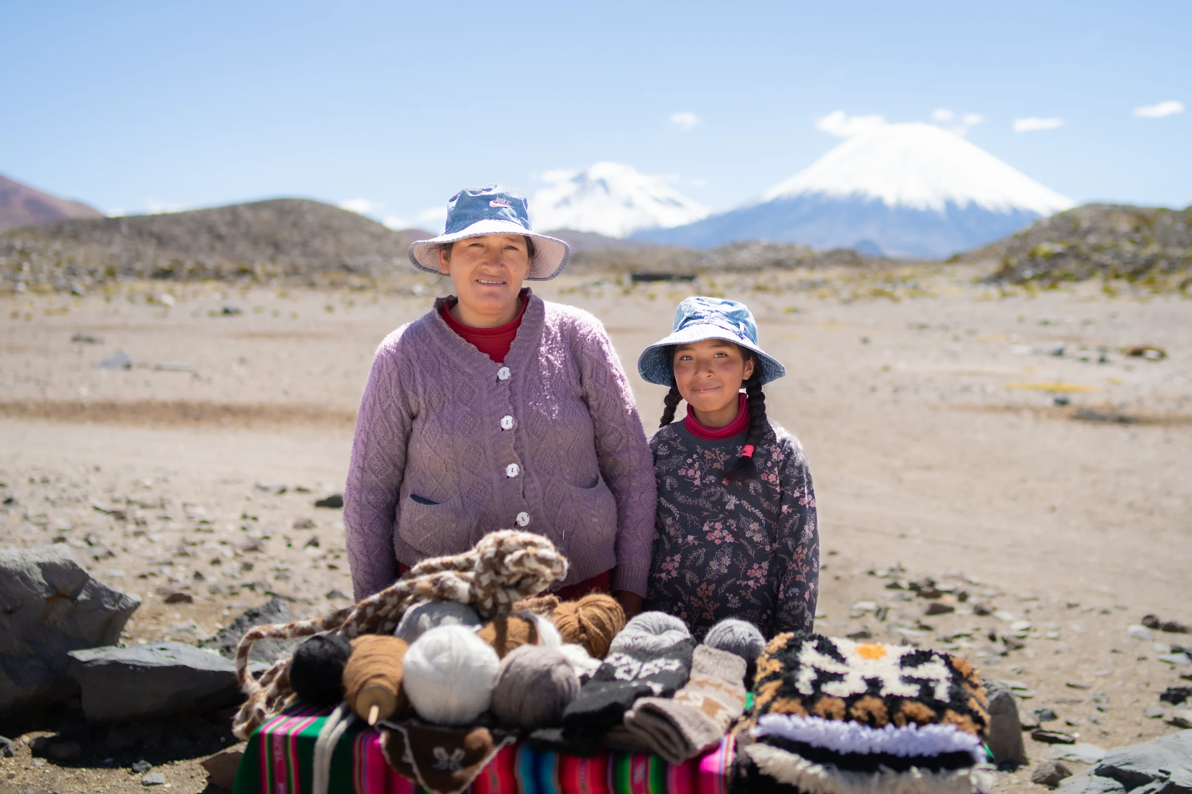 Mujer y niña junto a mesa con lanas artesanales en el altiplano