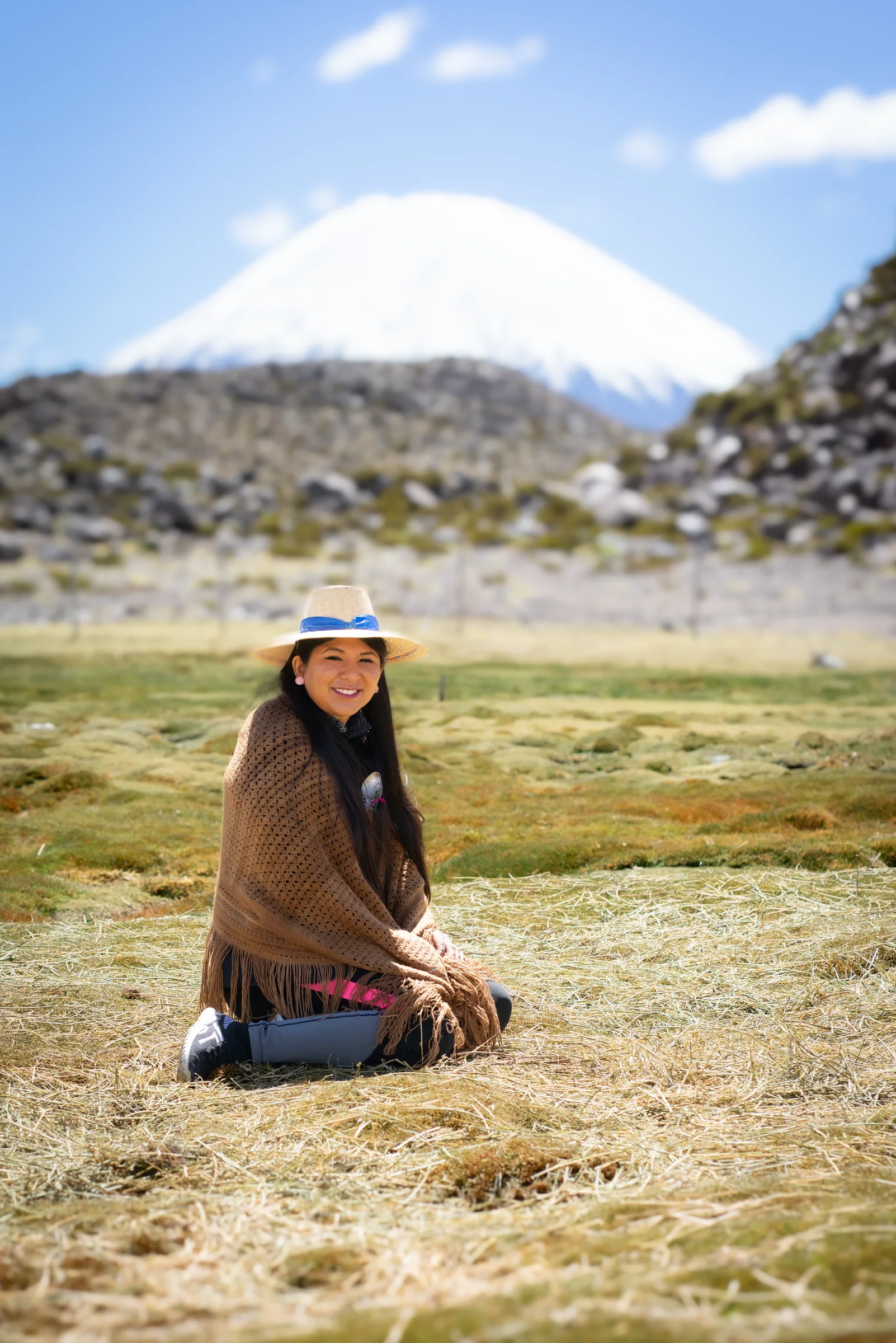 Mujer sentada en bofedal andino con montaña nevada al fondo