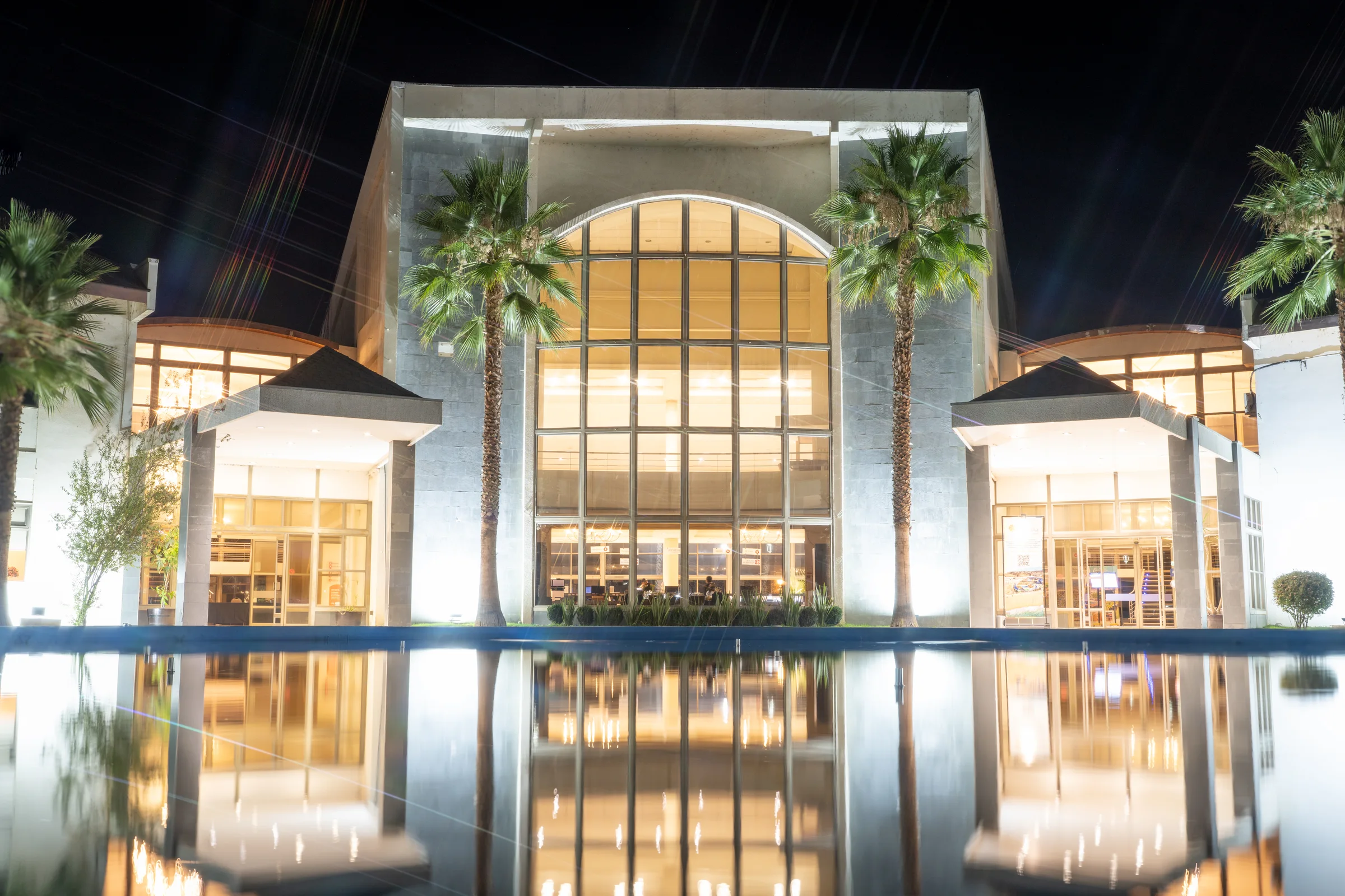 Centro de eventos iluminado de noche con reflejo en espejo de agua