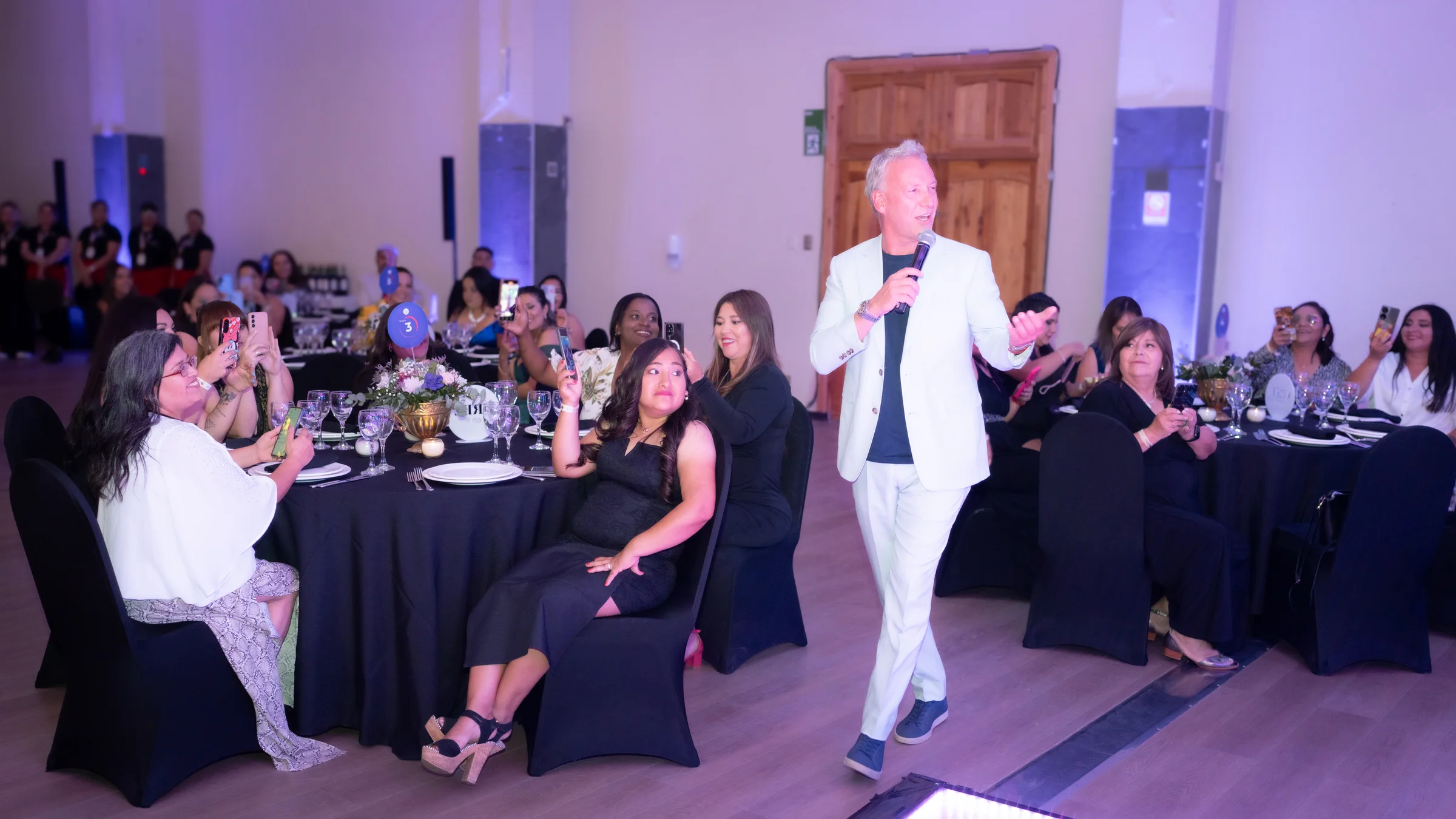 Presentador en salón dirigiéndose a los asistentes de una cena corporativa