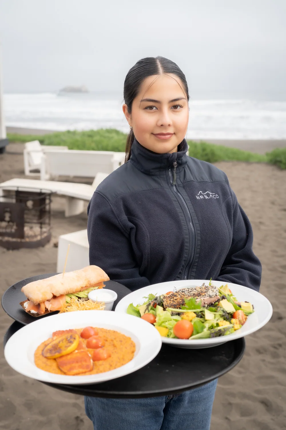 Mesera sosteniendo bandeja con preparaciones gastronómicas frente al mar