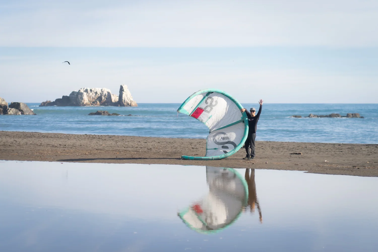 Deportista en la orilla de la playa con cometa de kitesurf y rocas marinas