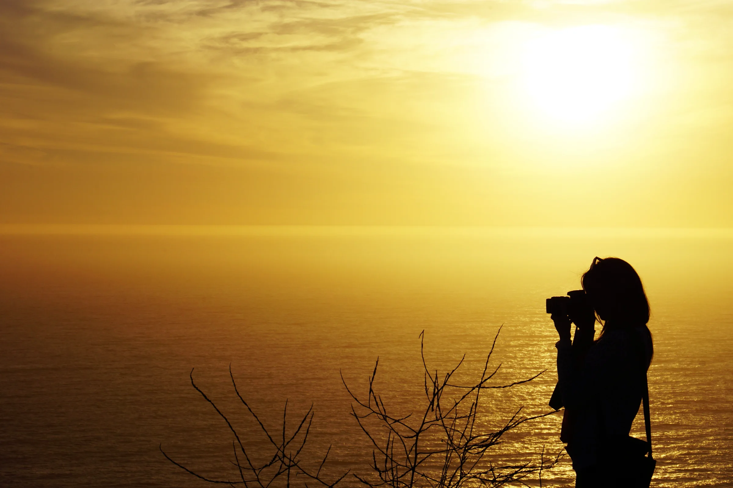 Silueta de fotógrafa capturando el atardecer frente al mar