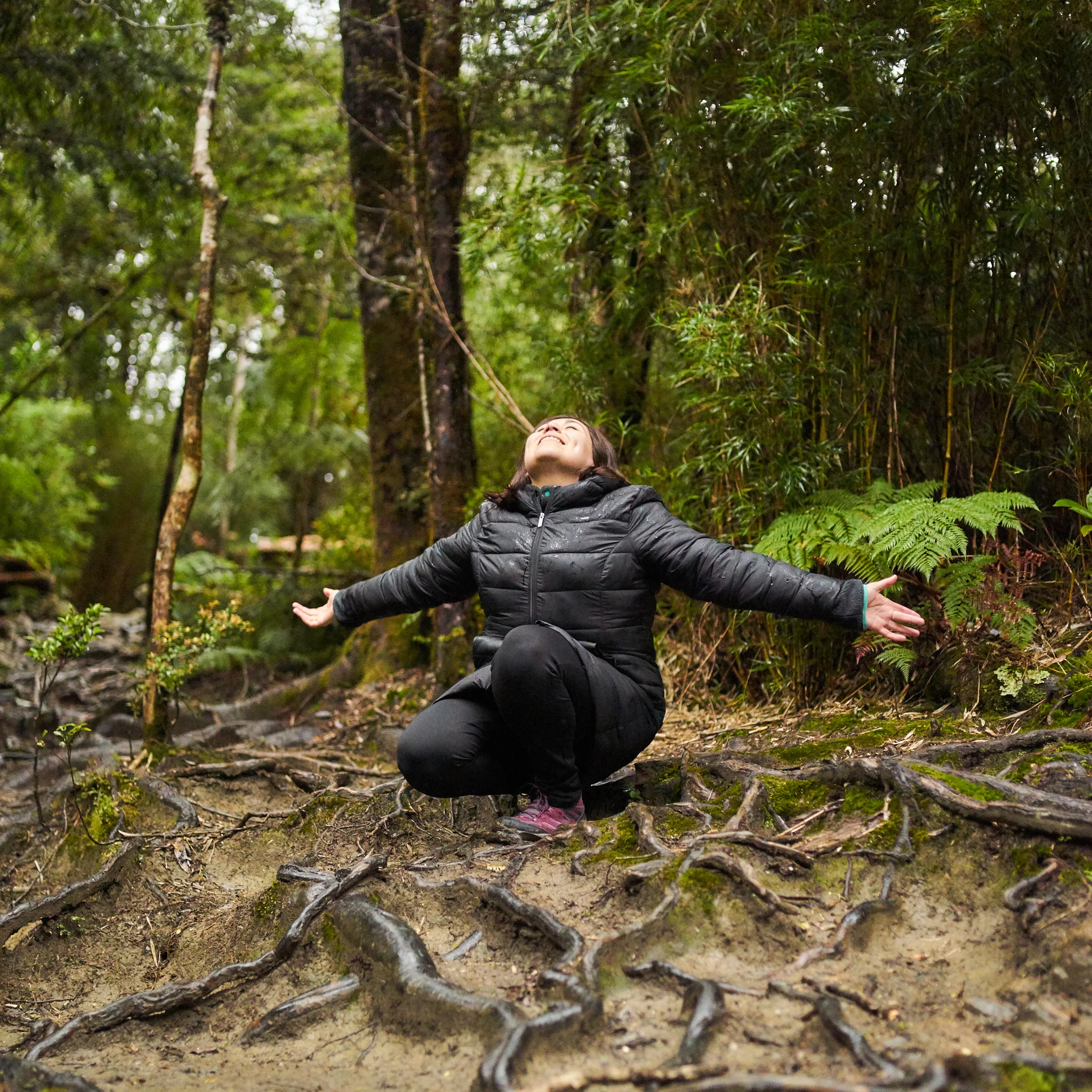 Persona descansando con brazos abiertos sobre raíces de árboles en el bosque