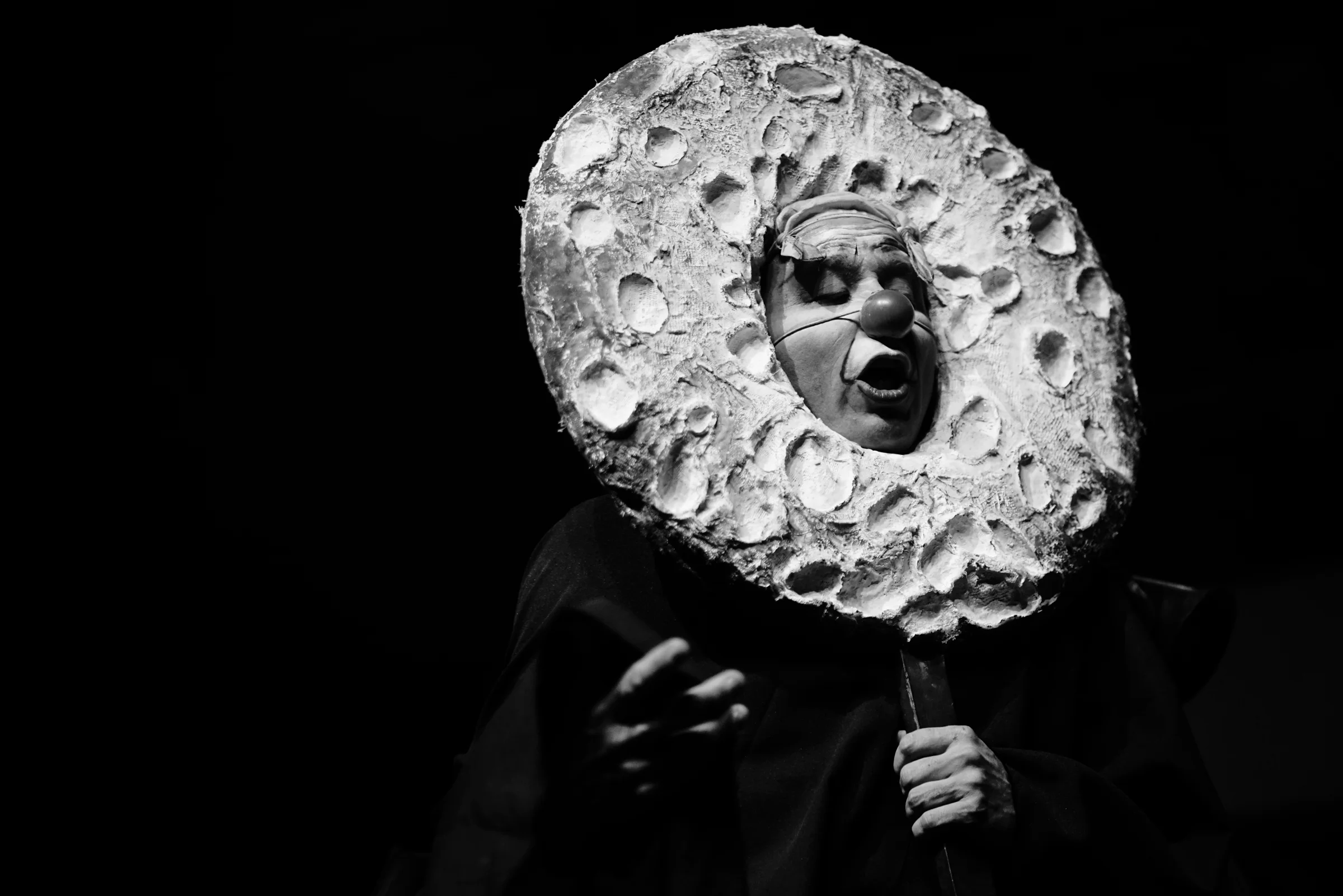 Actor caracterizado con máscara circular en montaje teatral