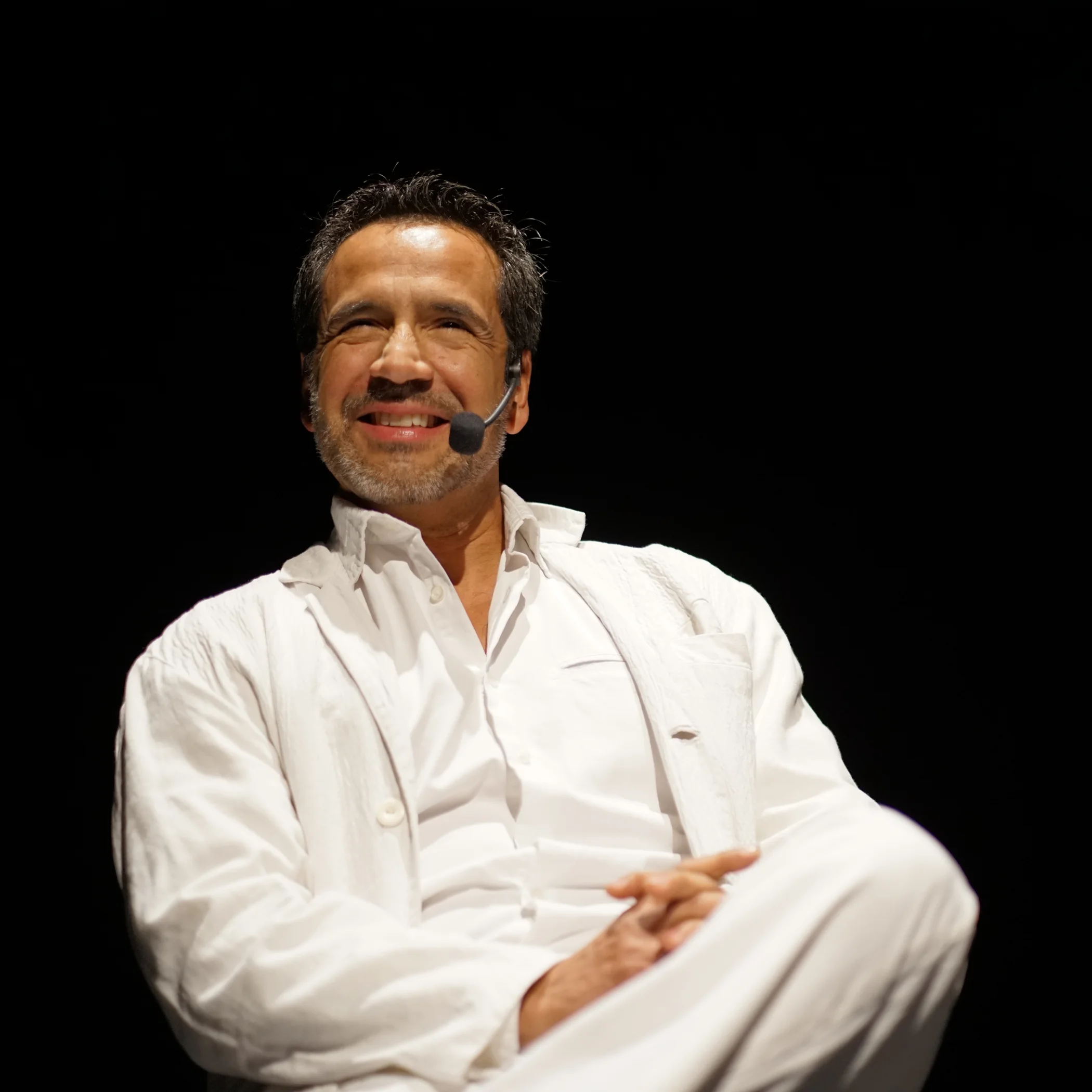 Actor con vestuario blanco y micrófono en obra de teatro